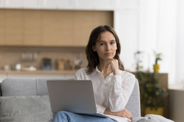 istock Pensive woman sits on sofa with wireless computer on laps 2171771370