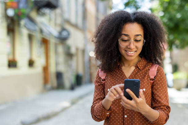 istock Young woman walking outside, using smartphone, and smiling 2171775196