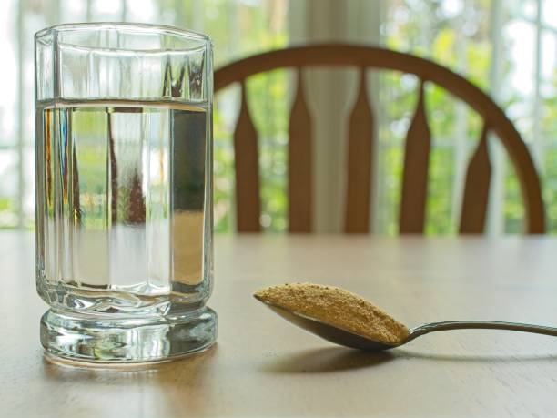 Fiber powder in spoon with glass of water, on wood table. Concept of psyllium husk fiber supplementation if not getting enough in regular diet.
