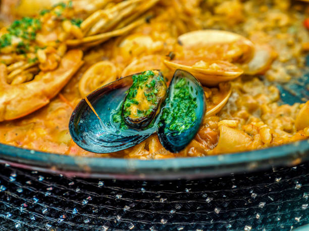 The traditional Spanish seafood dish called Paella in a black pan with clams and shrimp on a pad of rice
