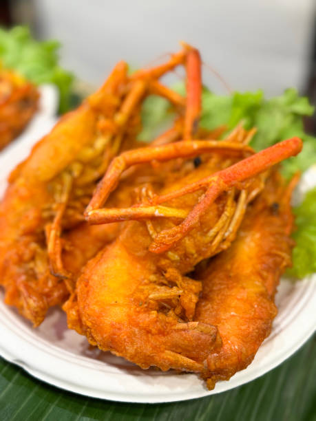istock Full frame image of single-use bowl of freshly cooked deep-fried battered seafood with lettuce, whole King prawns, banana leaf background, elevated view, focus on foreground 2171783614