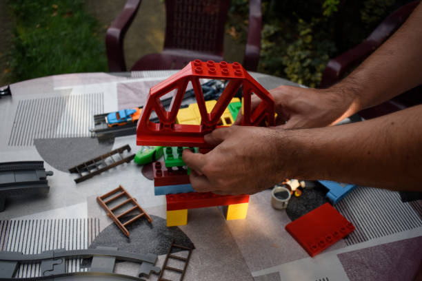A man assembling  toys on a garden table with colourful tablecloth in a garden.