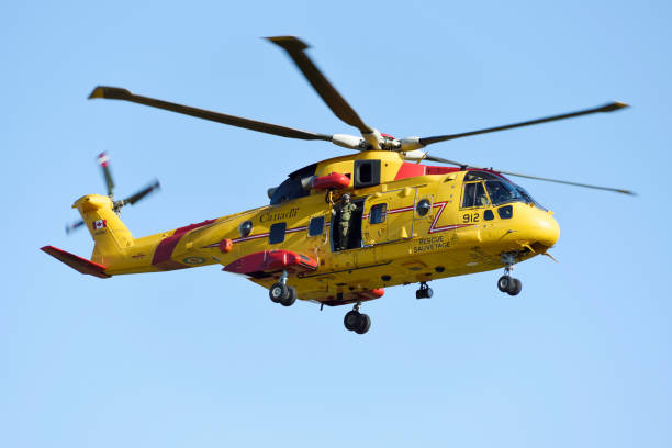 Canada, Fundy National Park - August 22, 2024: Yellow rescue helicopter of the Canadian armed forces with rescuer on a lookout from open door during a search and rescue operation in Fundy national Park, New Brunswick.