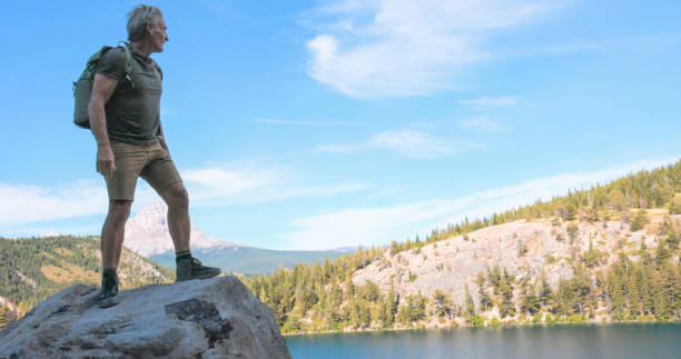 Mature man on boulder above lake, Crowsnest Pass, Canadian Rockies