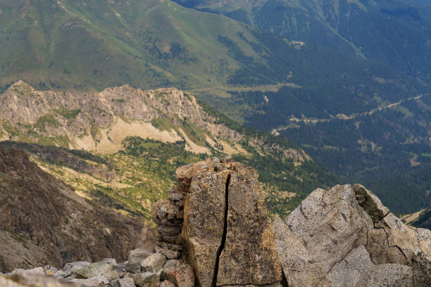 A close-up view of a rugged rocky outcrop with a vast, green mountain valley in the background.