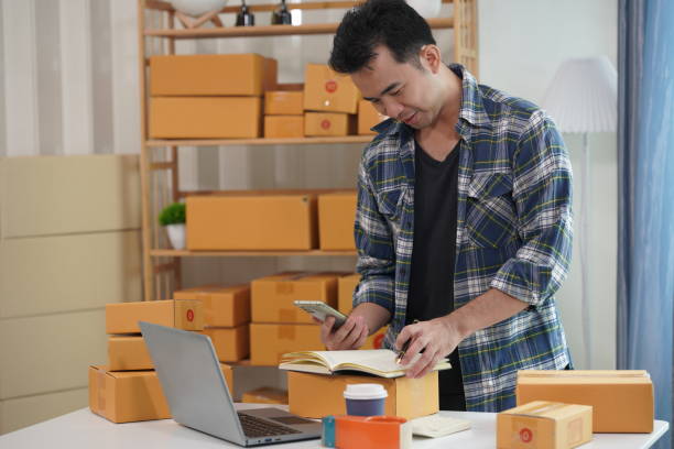 istock Small business owner starting up using smartphone and writing address on package box to send to customer. Concept of businessman doing ecommerce business on website and social media. 2171861533