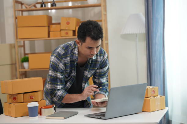 istock Small business owner starting up using smartphone and writing address on package box to send to customer. Concept of businessman doing ecommerce business on website and social media. 2171861546
