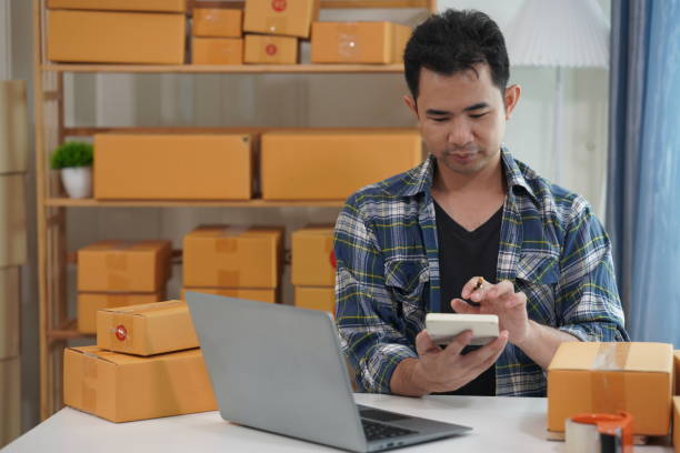istock Small business owner starting up using smartphone and writing address on package box to send to customer. Concept of businessman doing ecommerce business on website and social media. 2171861547