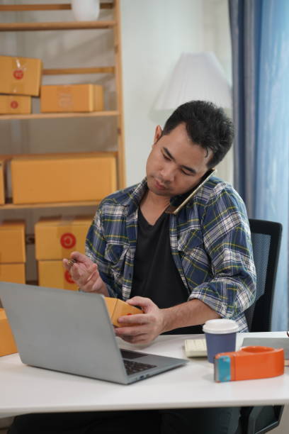 istock Small business owner starting up using smartphone and writing address on package box to send to customer. Concept of businessman doing ecommerce business on website and social media. 2171861552