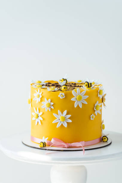 istock Birthday spring cake with yellow chocolate frosting decorated with edible sugar paste bees and white fondant chamomile flowers. White background 2171877793