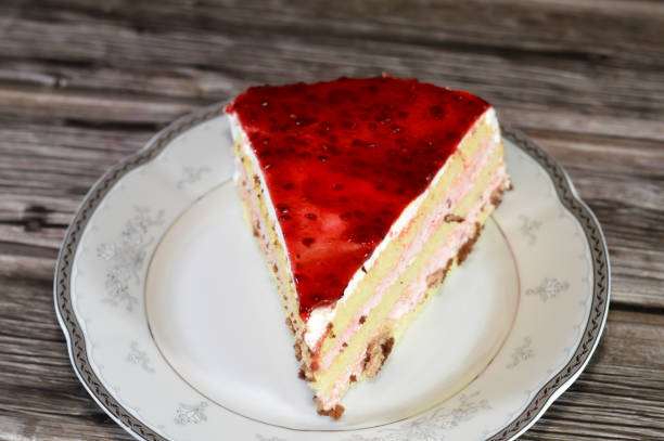 Berry triangular spongy cake piece filled and topped with layers of berries paste cream, with layers of cake, served in a plate and isolated on wooden background