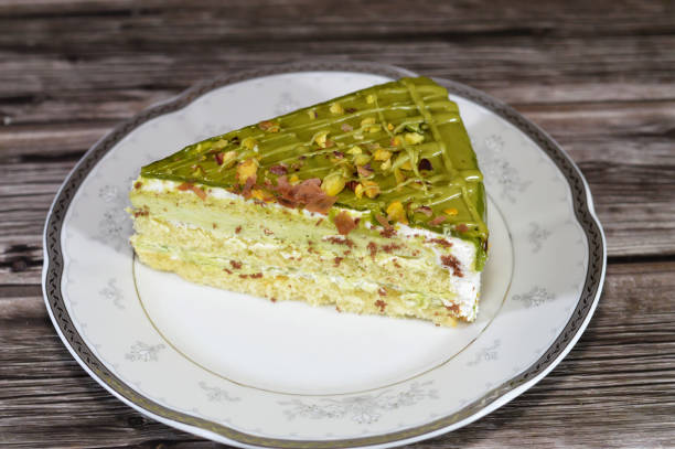 Pistachio triangular spongy cake piece filled and topped with layers of pistachio paste cream and pieces, with layers of cake, served in a plate