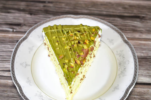 Pistachio triangular spongy cake piece filled and topped with layers of pistachio paste cream and pieces, with layers of cake