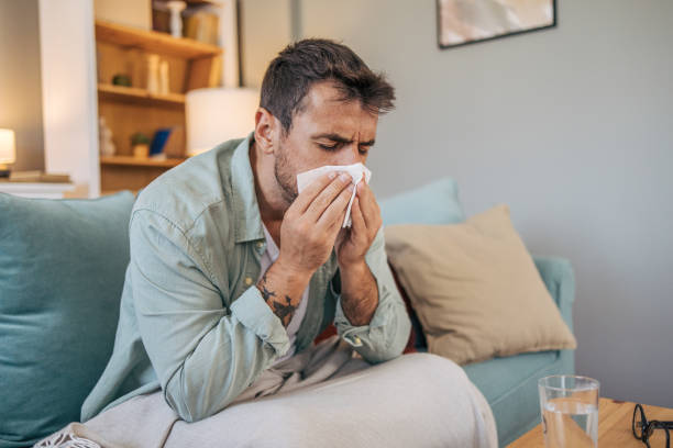 A sick mid adult man is sitting on a sofa.
