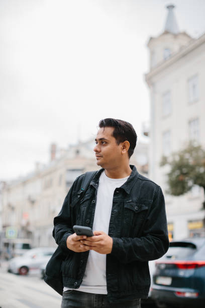 istock A young Indian man is standing with a backpack on a city street, using a mobile phone, reading and writing a message, making a phone call. 2171899096