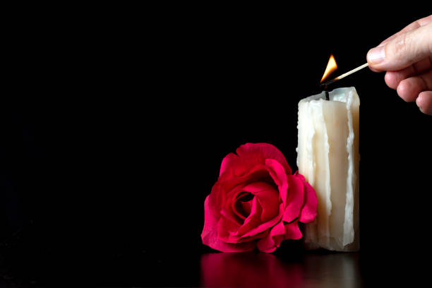 istock HAND LIGHTING A CANDLE WITH A MATCH NEXT TO A RED ROSE ON BLACK BACKGROUND. 2171910244