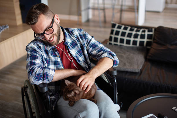 Man recovering at home with pet therapy Qurantine, stay home, rehabilitation concept. Portrait of young man in wheelchair petting a cat sitting on his lap weak cat stock pictures, royalty-free photos & images
