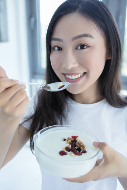 Young and happy woman is eating fresh yoghurt with a passion nuts and fruit for breakfast