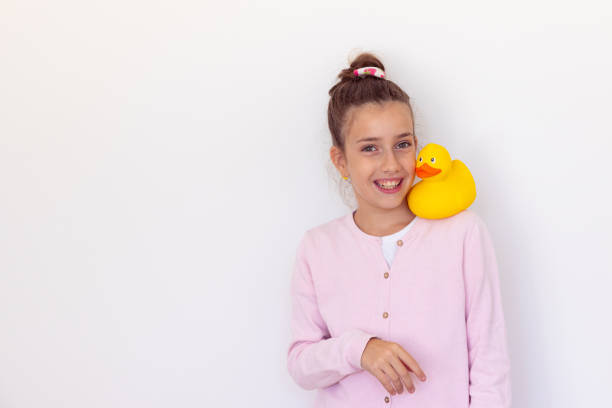 Smiling ear to ear girl proudly showing her yellow duck toy in front of white wall