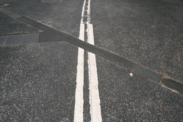 Old faded double white lines in the middle of a road in bad condition.
