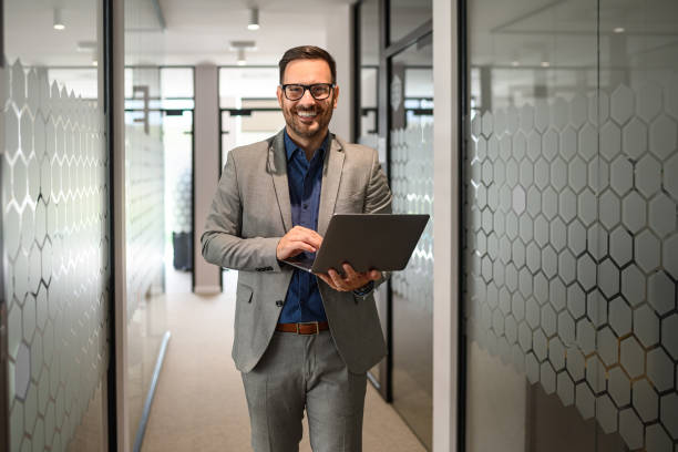 istock Successful young businessman in eyeglasses working on his computer while walking in office corridor 2171932936