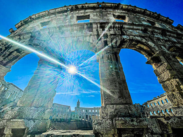 Visitors admire the impressive architecture of the Roman amphitheater in Pula Croatia basking in the sunlight on a clear day surrounded by history.