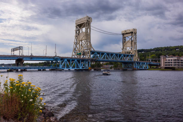 A double deck lift bridge crossing a river between towns with a boat heading towards the bridge.