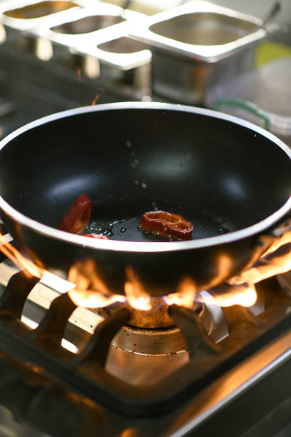 A chef cooks red peppers in a hot pan using tongs in the hotel kitchen, showcasing the art of cooking with fresh ingredients