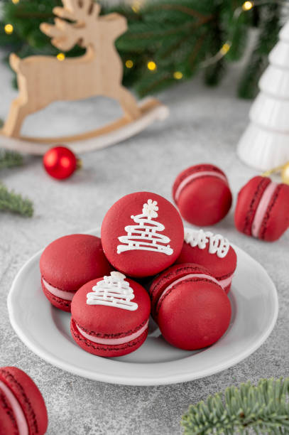 Christmas raspberry macarons decorated with sugar glaze on a white plate on a concrete background. Festive dessert. Top view.