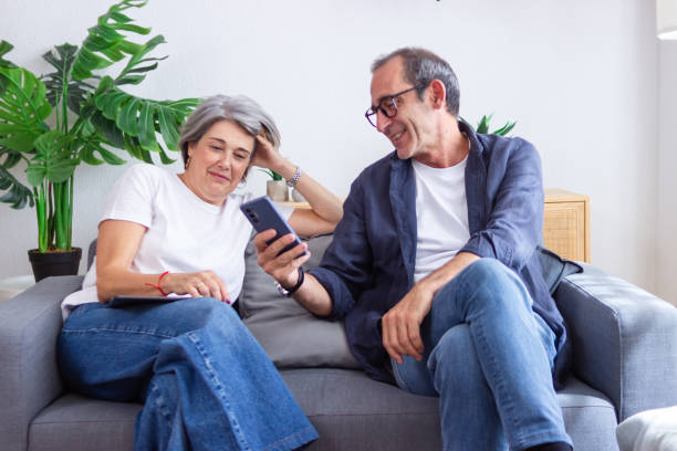istock Senior couple relaxing on sofa at home browsing internet on smartphone 2171980570