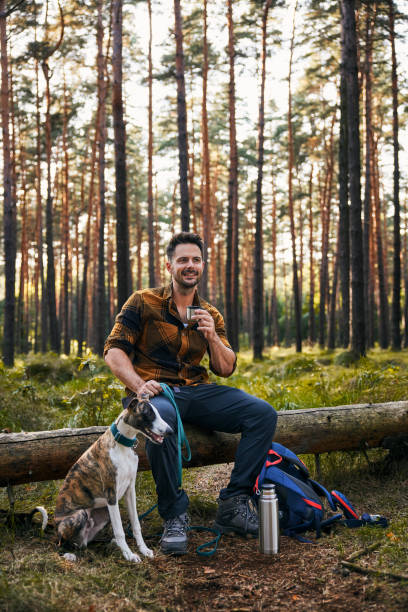 istock Man with dog resting in forest during autumn hike drinking from thermos 2171993349