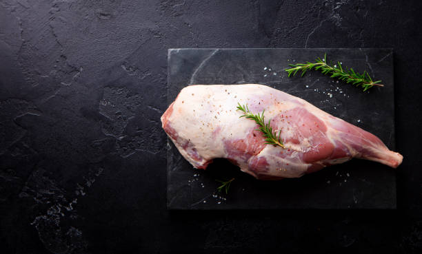 istock Raw lamb leg with spices and herbs on marble cutting board. Dark background. Top view. Copy space. 2171997362