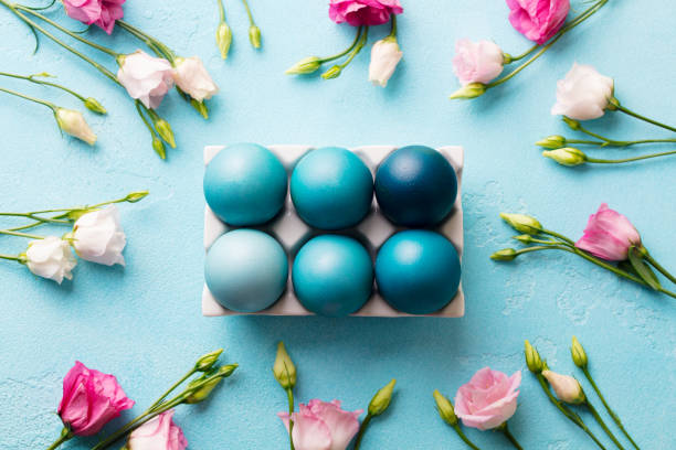 istock Colorful Easter eggs in porcelain egg box with pink eustoma flowers. Blue background. Top view. 2171997407