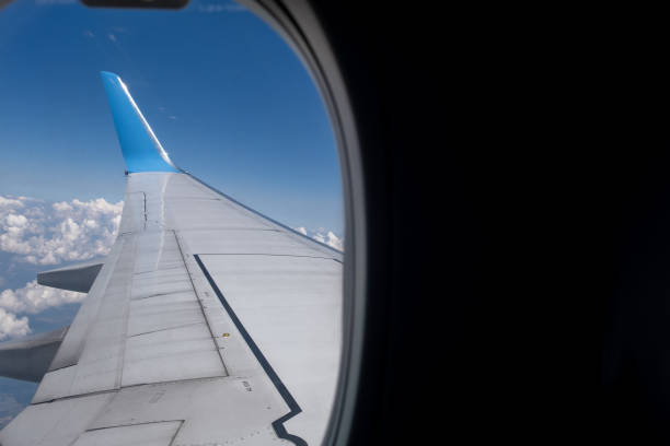 Looking through an airplane window at the aircraft wing during a mid-flight Looking through an airplane window at the aircraft wing during a mid-flight with clouds and blue sky in the background aircraft point of view stock pictures, royalty-free photos & images