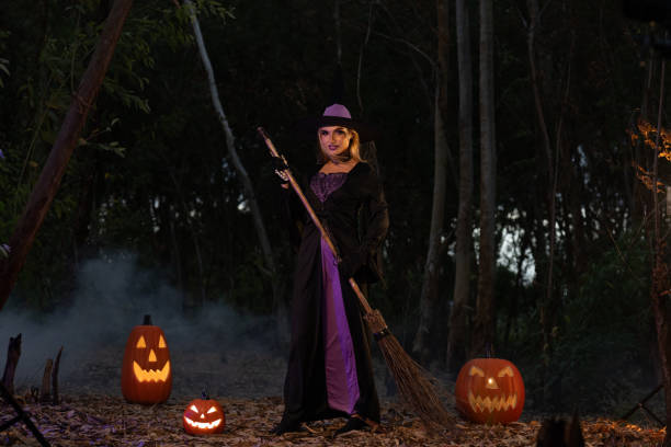 istock A young witch with jack o'lantern in a night misty forest. Smiling attractive woman with a carved pumpkin and smoke. Halloween party, trick or treat concept. Magic, witchcraft, sorcery. Banner with copy space 2172002602