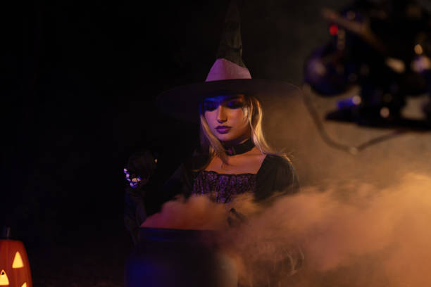 A young witch with jack o'lantern in a night misty forest. Smiling attractive woman with a carved pumpkin and smoke. Halloween party, trick or treat concept. Magic, witchcraft, sorcery. Banner with copy space