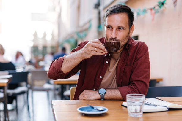 Man drinking coffee at a lively outdoor cafe scene.