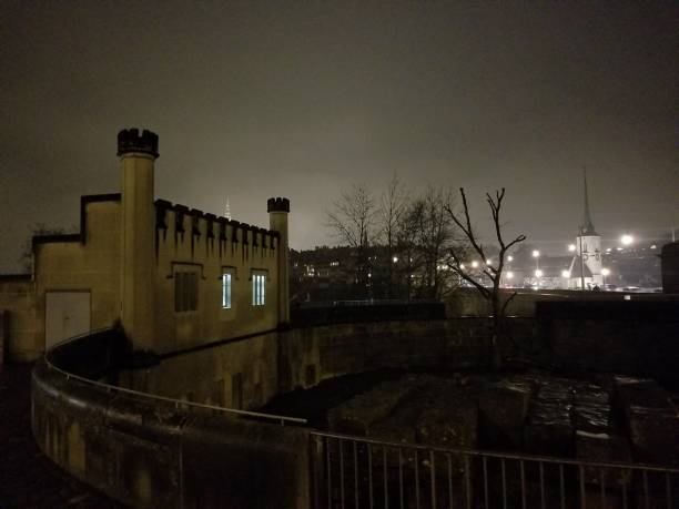 A dimly lit view of Bern's old buildings showcases their architectural details against a foggy night. The skyline is punctuated by faint lights in the distance.