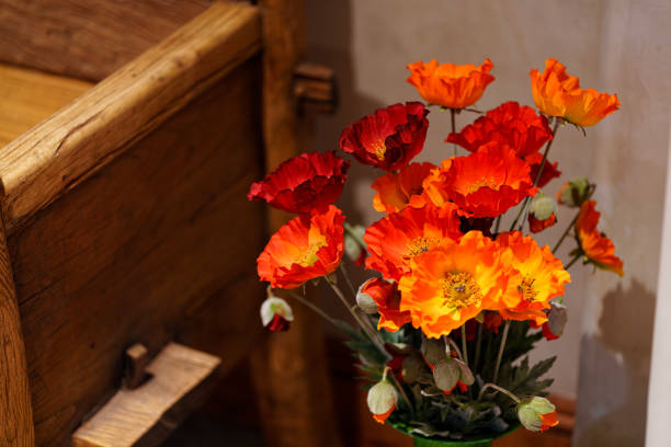 Orange Artificial Flowers in Vase Home Decor Detail - Selective focus on flowers next to wooden bench home interior design detail. Soft defocused background.