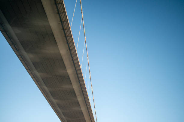 A steel bridge arch stretches against a vivid blue sky dotted with soft, white clouds, showcasing modern engineering amidst a serene atmosphere during daylight.