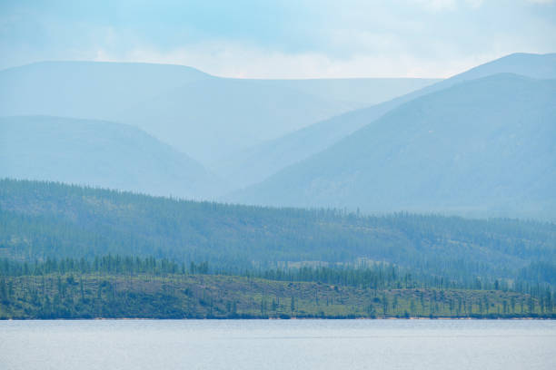 A tranquil lake stretches out towards misty, layered mountains in the background, creating a peaceful and atmospheric landscape.