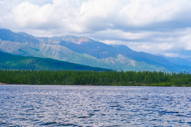 A tranquil lake with smooth waters reflects the soft light of a misty morning, framed by distant mountains and a tree-lined shore, creating a serene and peaceful landscape.