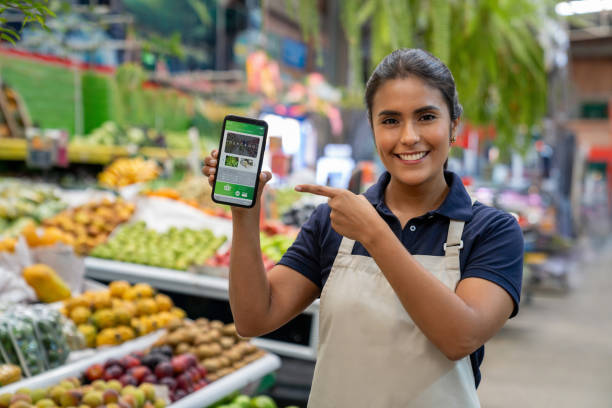 istock Food market vendor pointing at a mobile phone with an e-commerce app on display 2172032074
