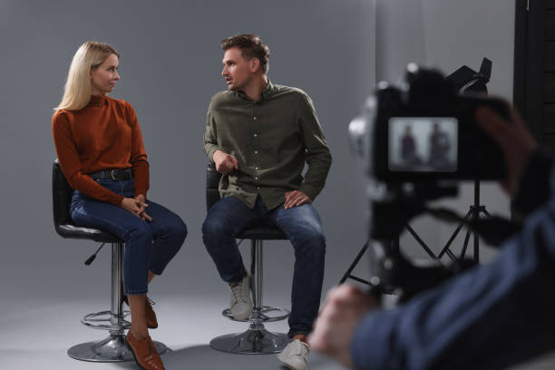 Close up shot of digital camera on tripod recording interview. Young businesswoman giving interview to male journalist, sitting and talking in TV show studio. Television, mass media, TV show concept.