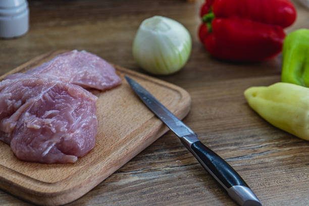 A piece of chicken fillet on a cutting board, a knife and vegetables on the side High quality photo.