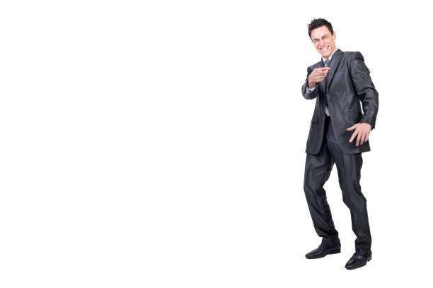 Full body of happy male executive manager pointing at camera and laughing on funny joke in studio against white background