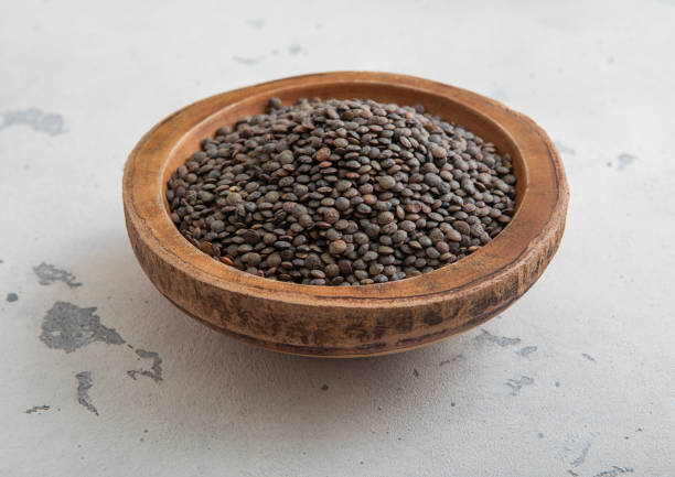 Raw dry black lentils seeds in wooden bowl on light table.