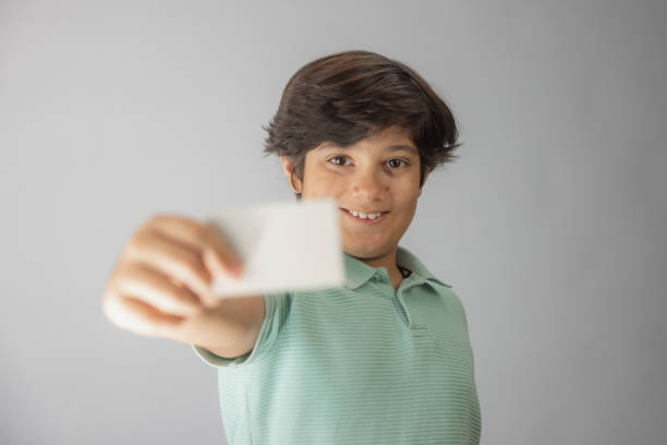 istock Young multiracial boy Indian-Iranian looking at camera holding a blank credit card 2172102568
