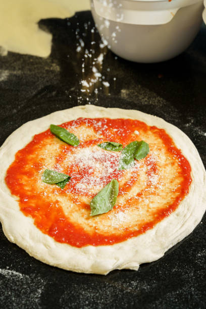 istock A chef preparing a pizza with tomato sauce and spreading parmesan cheese 2172103761