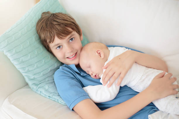 Child watching newborn baby in bassinet. Sibling meeting new family member. Kids play in white bedroom. Nursery crib bedding and textile for young kid. Siblings love.
